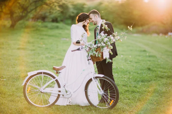 Casal romântico comemorando seu casamento no parque ensolarado com bicicleta decorada entre eles. Sinalizadores de sol quentes — Fotografia de Stock