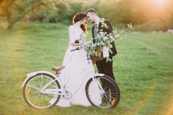 Casal romântico posando no parque ensolarado com bicicleta decorada. Sinalizadores de sol quentes — Fotografia de Stock