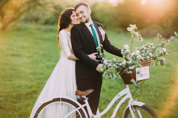 Romantic young couple posing in sunny park with decorated bicycle. Warm sun flares