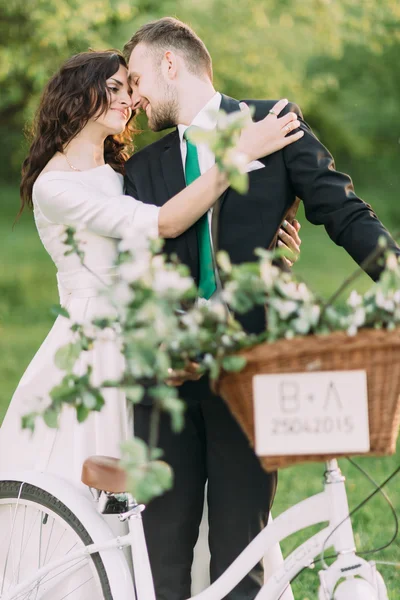 Romântico jovem casal beijando no parque ensolarado encostado na bicicleta decorada — Fotografia de Stock