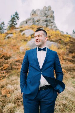 Yakın çekim yakışıklı şık damat ile arka plan olarak bir kayalık doğal manzara mavi elbiseli portresi