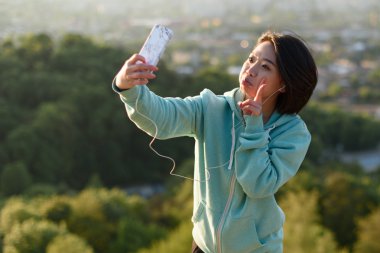 Selfie çekici ve Komik suratlar telefonunu kullanarak Park'ta açık yapma güzel Japon bayanı. Bulanık şehir arka plan