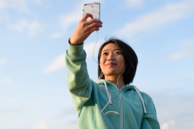 Kısa saçlı selfie telefonunu kullanarak açık çekici şehvetli Japon kadın portresi. Mavi bulutlu gökyüzü arka plan