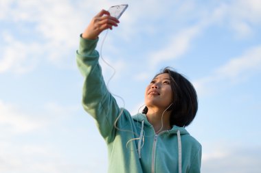 Selfie telefonunu kullanarak açık alarak kısa saçlı güzel Japon kadın portresi. Mavi bulutlu gökyüzü arka plan