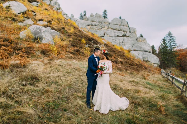 Hermosa pareja de boda en idílico paisaje pastoral con rocas y valla como telón de fondo —  Fotos de Stock