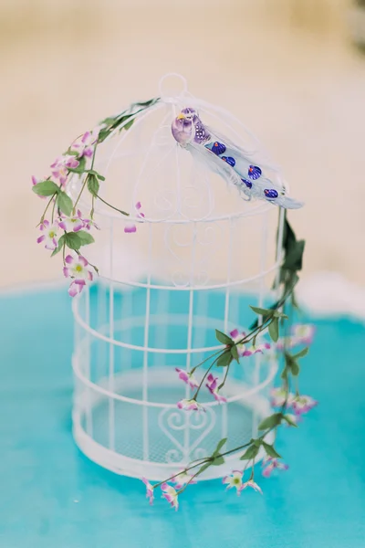Primer plano de hermosa jaula decorativa para pájaros con algunas flores lindas aisladas en la mesa cubierta por mantel turquesa — Foto de Stock