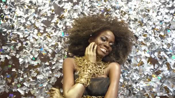 Creatieve surrealistisch portret van sexy Afro-Amerikaanse vrouwelijke model met gouden glanzend make-up gezicht kunst. Zilver glanzend confetti achtergrond — Stockvideo