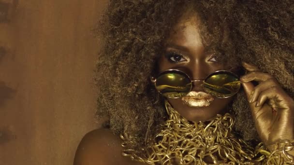 African american female model in massive sunglasses with bright glitter makeup, glossy golden hairstyle and big red lips posing on the black studio background. Vogue fashion concept — Stock Video