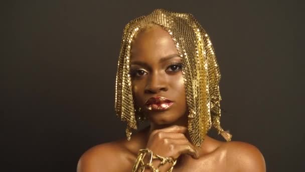 Nahaufnahme surreales Porträt einer glänzenden afrikanisch-amerikanischen Frau mit leuchtend goldenem Make-up und Kopfbedeckung. Bronze-Karosseriefarbe — Stockvideo