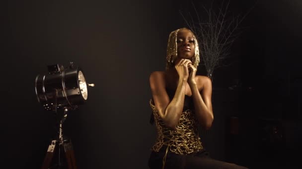 Sexy ritratto lussuoso di sexy modello afroamericano femminile con lucido trucco dorato e copricapo lucido in posa per la fotocamera. Vernice del corpo in bronzo, sfondo nero studio — Video Stock