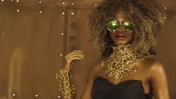 Parlak glitter makyaj, parlak altın saç modeli ve stüdyo arka planda poz büyük kırmızı dudaklar ile büyük güneş gözlüğü Magic gerçeküstü altın afro-amerikan kadın modeli — Stok video
