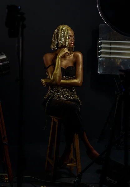 Surrealistische portret van sexy Afro-Amerikaanse vrouw met glanzende gouden make-up en hoofddeksels poseren voor de camera in Studio. Bronzen bodypaint, zwarte studio achtergrond — Stockfoto