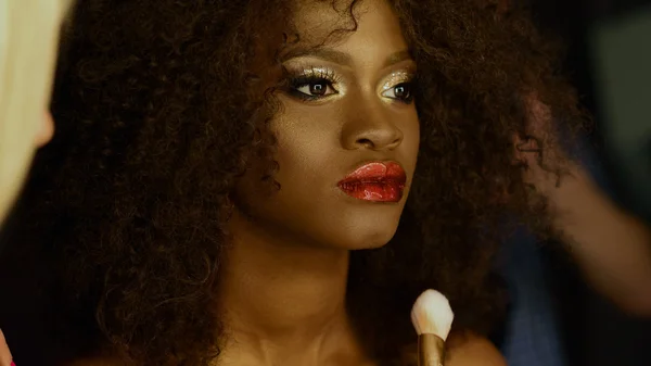 Surrealistische portret van Afro-Amerikaanse model met heldere gouden glitter make-up en glanzende kapsel voorbereiden voorschieten op de stylist — Stockfoto