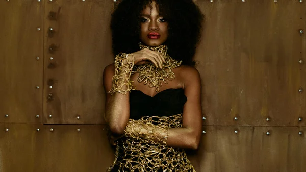 Luxe portret van sexy Afro-Amerikaanse vrouwelijke model met glanzende gouden make-up poseren voor de camera op de achtergrond van de textuur Studio — Stockfoto