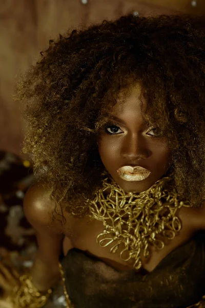 Portrait surréaliste de sexy modèle féminin afro-américain avec un maquillage doré brillant posant sur l'appareil photo sur le fond du studio. Concept de mode sauvage — Photo