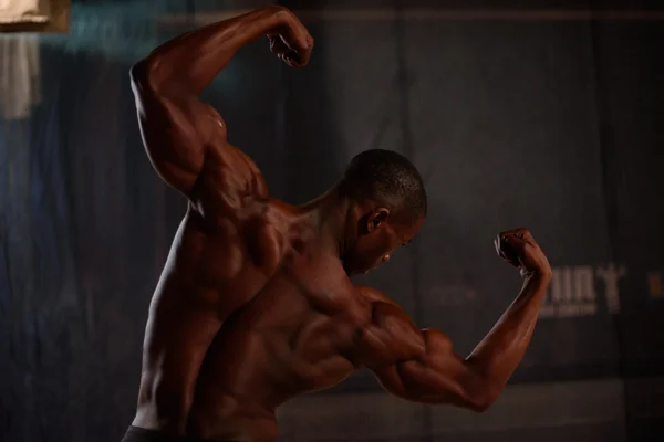 Africano americano construtor de corpo masculino posando em um fundo preto em estúdio. Visão traseira — Fotografia de Stock