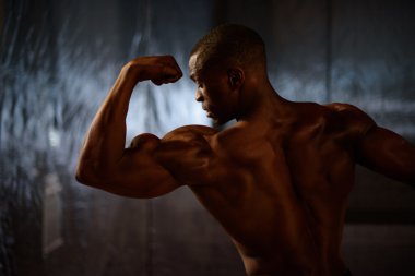 Siyah Afrika kökenli Amerikalı fitness modeli gösteren kaslar studio arka planda yan görünüm