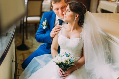 Sevgi dolu şık giyimli damat yavaşça yeni karısı güzel beyaz elbisenin içinde öpüşme