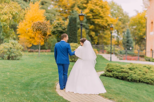 Frisch verheiratete Paare spazieren im Park. Bräutigam hält sanft Hand seiner eleganten Braut — Stockfoto