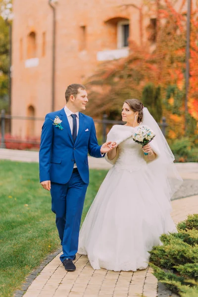 Casamento recém-casado a passear no parque. quarto amoroso é gentilmente segurando a mão de sua noiva elegante — Fotografia de Stock