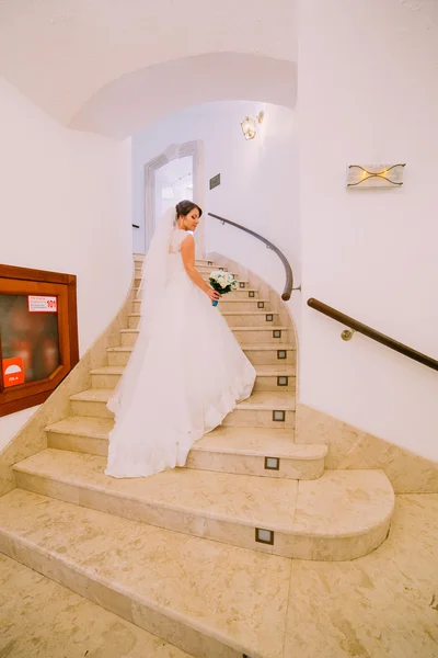 Bela noiva em vestido de casamento branco longo subindo escadas com interior de luxos — Fotografia de Stock