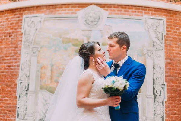 Щаслива наречена і наречена цілуються на тлі красиво прикрашеної стіни з червоної цегли — стокове фото