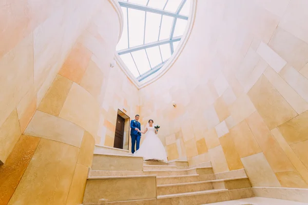 Casal recém-casado amado em escadas de mármore com paredes de arenito no fundo. ângulo baixo — Fotografia de Stock