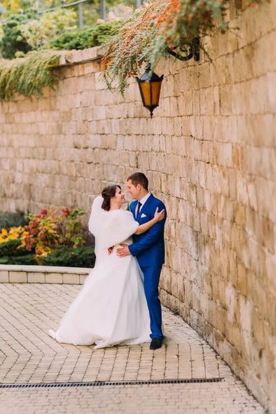 Elegante bella coppia di nozze, sposa allegra e amorevole sposo vicino muro di arenaria — Foto Stock