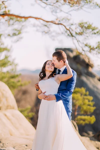 Jonge romantische jonggehuwde paar knuffelen in zonlicht op rotsachtige klip — Stockfoto