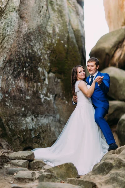 Joven y hermosa novia con su elegante novio bailando en la hendidura de roca envejecida — Foto de Stock