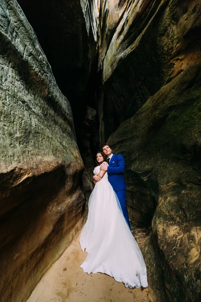 Giovane e romantica sposa con il suo sposo amorevole posa in fessura roccia oscurata — Foto Stock