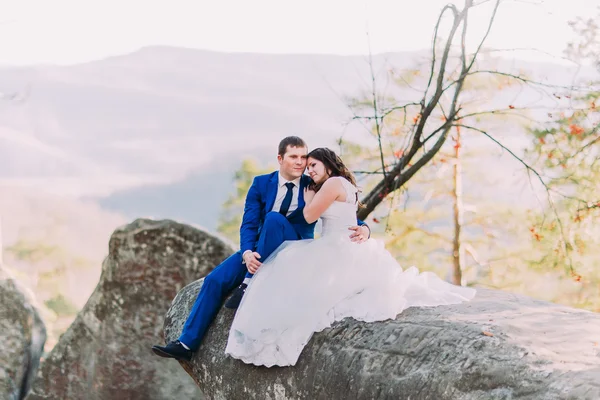 Romantique couple nouvellement marié assis sur le bord des rochers, mariée robe écartant le rocher. Paysage des collines — Photo