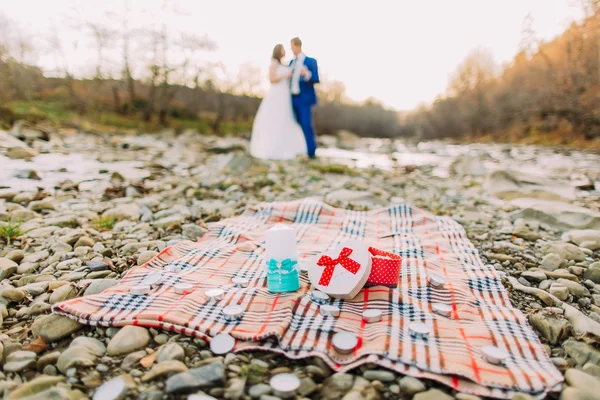Романтична молода весільна пара п'є вино на гальковому березі річки з пагорбами і струмком як фон — стокове фото