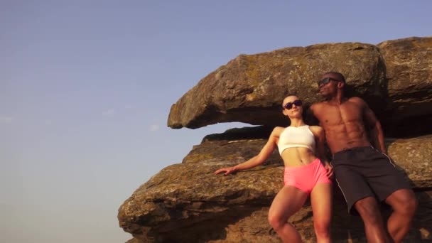 Sexy fit mixed race couple with perfect bodies in sportswear posing on the rocky mountains landscape. Sport and lifestyle concept — Stock Video