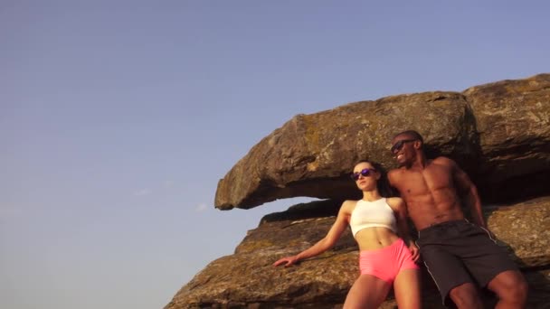 Sexy pareja de carreras mixtas en forma con cuerpos musculares perfectos en ropa deportiva posando en el paisaje de las montañas rocosas . — Vídeo de stock