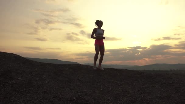 Silhouet van fit vrouw loper met perfecte gespierd lichaam jogging buiten op de zonsondergang. Berg landschap-achtergrond — Stockvideo