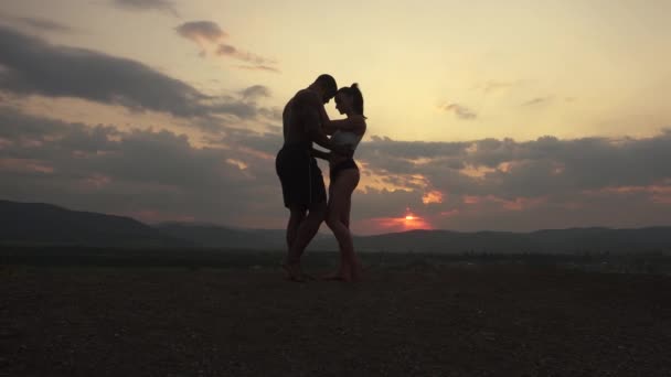 Siluetas de pareja atlética muscular de instructores de fitness posando al atardecer en la cima de la montaña. Hermoso cielo nublado fondo — Vídeo de stock