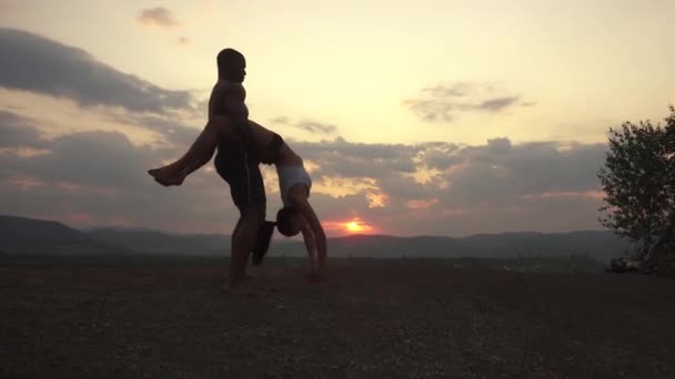Schönes athletisches muskulöses Mischlingspaar, das bei Sonnenuntergang auf dem Berggipfel Gymnastikübungen macht. wunderbare bewölkten Himmel Hintergrund. — Stockvideo