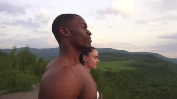 Sidovy av en fitness muskulös blandade Race par tittar på soluppgången i bergen tillsammans. Skönhet och perfektion av människor förkroppsligar — Stockvideo