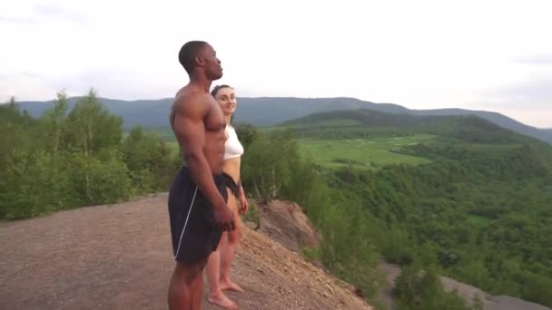 Momento de armonía. Feliz pareja de raza mixta atlética mujer caucásica y afroamericana culturista tomados de la mano y sonriendo juntos en la cima de la montaña — Vídeos de Stock