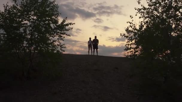 Vue de dos sur les silhouettes d'un couple sportif mixte et musclé regardant le lever du soleil dans les montagnes ensemble et se tenant la main . — Video