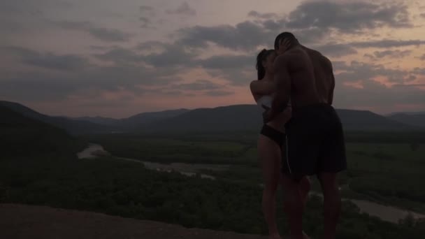 Siluetas de pareja atlética musculosa de raza mixta observando el amanecer en las montañas juntas y tomados de la mano. Impresionante paisaje de montaña fondo — Vídeos de Stock