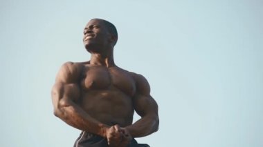 Açık mavi gökyüzü arka plan onun mükemmel kasları gösteren çıplak gövde ile Güçlü yakışıklı afro-amerikan vücut geliştirmeci