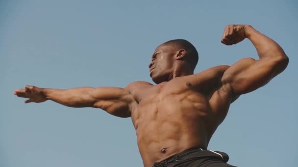 Sterke knappe African American bodybuilder toont zijn perfecte spieren op de heldere blauwe hemel achtergrond — Stockvideo