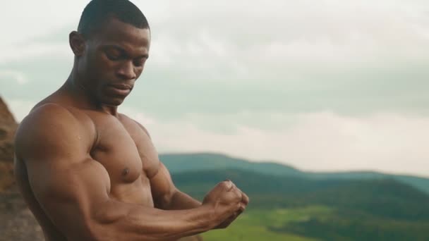 Close-up van gespierde Afro-Amerikaanse atletische man met naakte torso toont zijn spieren. Groene berg natuur achtergrond — Stockvideo