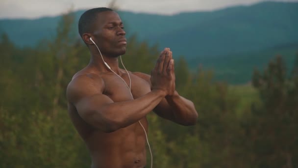 Muscular Africano americano construtor de corpo com as mãos de oração que se estendem sobre o pico da montanha durante o seu treinamento ao ar livre manhã. O sol nasce no céu. Momento de harmonia e felicidade — Vídeo de Stock