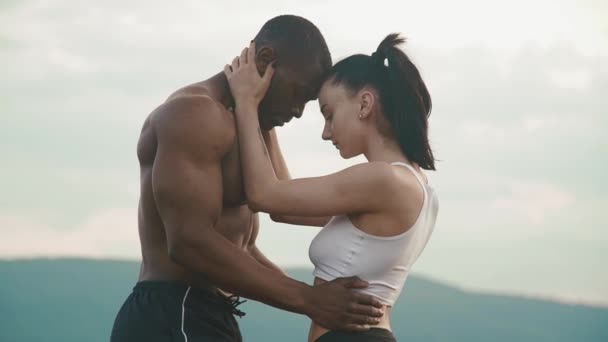 Sexy ajuste misto casal de raça com corpos perfeitos em sportswear suavemente abraçando no fundo paisagem montanhas . — Vídeo de Stock