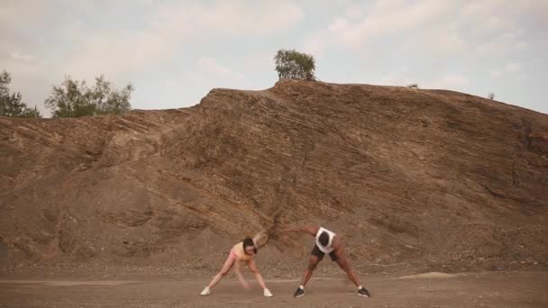 Fit ανάμεικτο ζευγάρι αγώνων κάνει άσκηση υπαίθρια στην πέτρινη παραλία. Σέξι μελαχρινή γυναίκα που εκτείνεται με την προσωπική γυμναστική μαύρος Αφρικανός Αμερικανός άνθρωπος — Αρχείο Βίντεο
