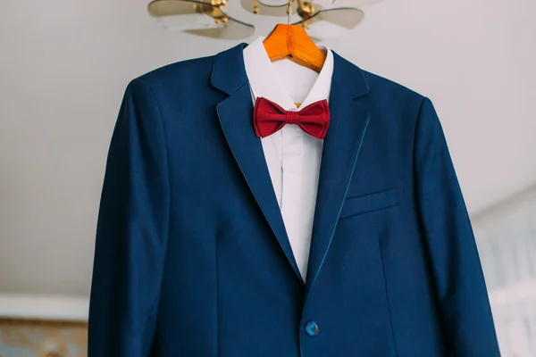 Close-up of excellent expensive blue suit with red bow-tie hanging on luster — Stock Photo, Image