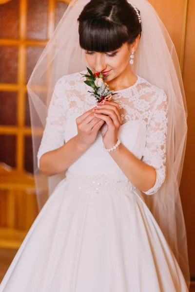 Beautiful bride smells cute floral boutonniere in dressing room before wedding — Stock Photo, Image